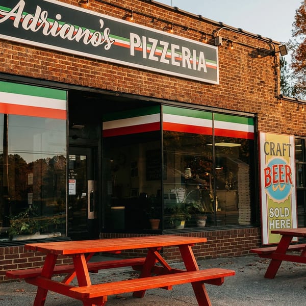 Adriano's Pizzeria storefront with red picnic tables outside, brick facade, and Italian flag colors.