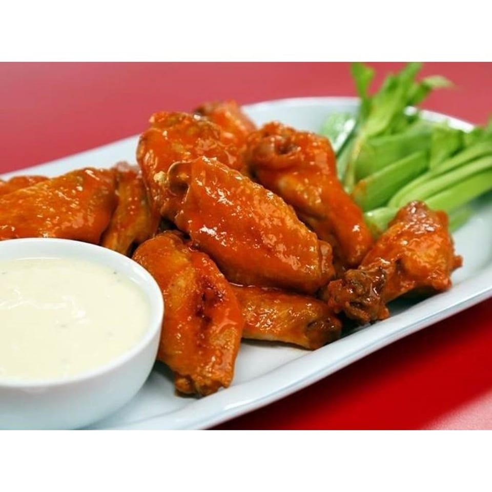 Glazed chicken wings arranged on a white platter with creamy dipping sauce and celery sticks.